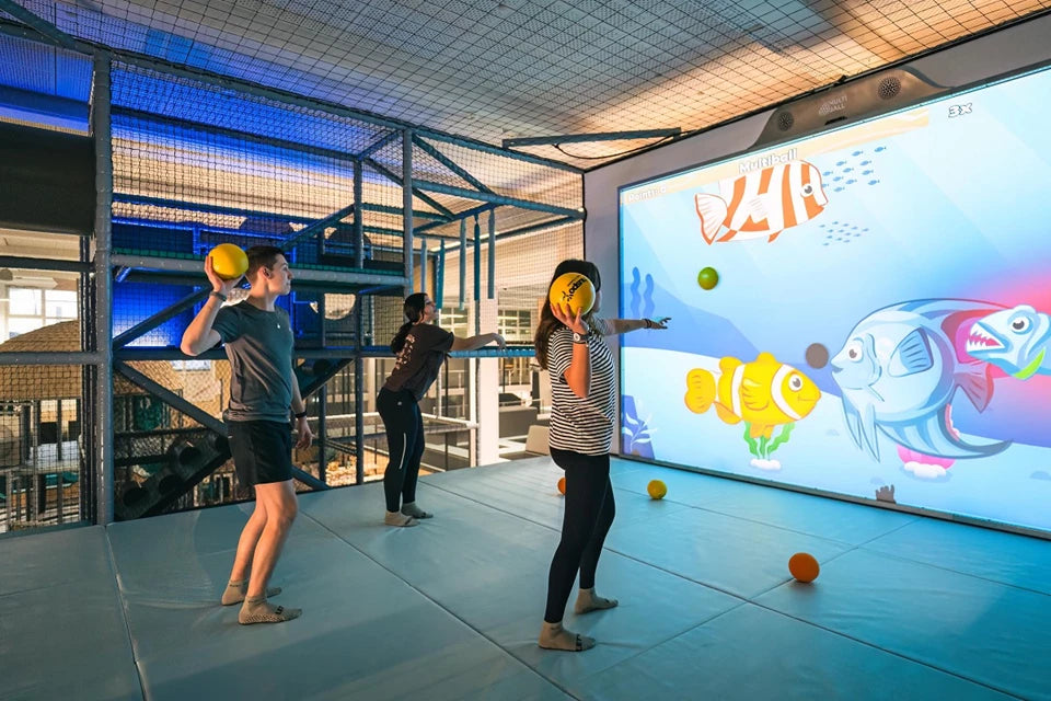 Children in the Swiss Holiday Park playing with colorful balls in front of the large MultiBall wall displaying animated fish.