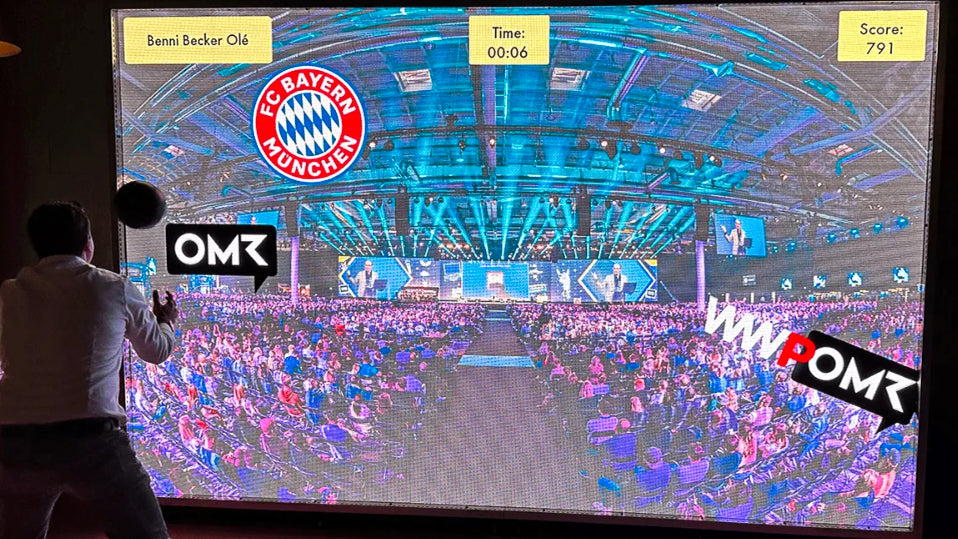 Two players interact with a digital MultiBall wall during a competitive socializing event, with branded games and a dynamic stadium background.