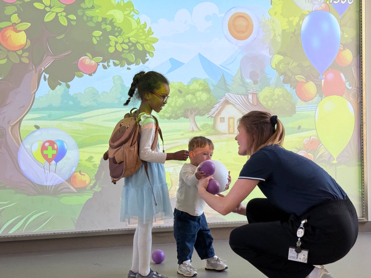 Two children at the Kinderklinik Schwabing München grabbing softballs from a sports therapist to play the Ballon Mania game on MultiBall
