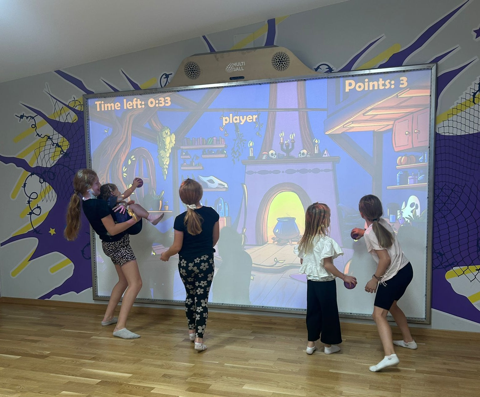 Children getting active by playing a Ghost Hunt game on the large interactive sports wall MultiBall in a room with colorful walls.