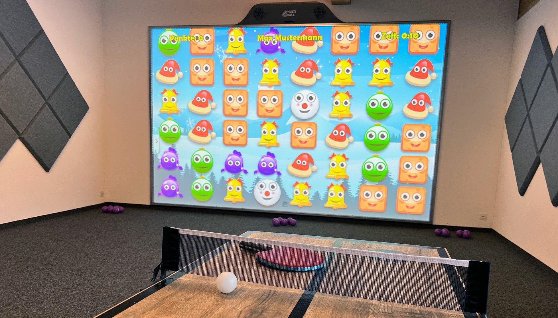 The interactive sports wall MultiBall in the kids play area in the Hotel Prada Resorts Brigels in Switzerland with the Winter Match game activated. Soft balls are on the ground and a mini table top tennis is in the front of the room.