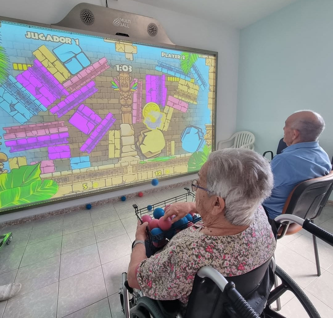 A old woman in a wheelchair and a senior playing games on MultiBall at the senior living residencia nuevaesperanza
